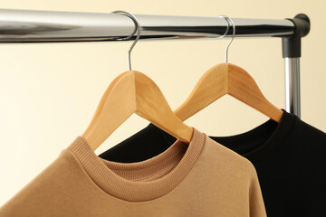 Hangers with stylish sweatshirts on beige background