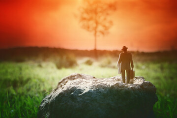 Surreal image of mysterious man walking alone in field during sunset