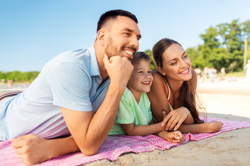 family, leisure and people concept - happy mother, father and son lying on summer beach