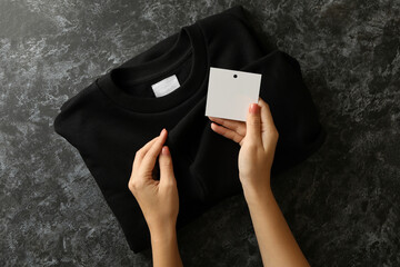 Female hands hold sweatshirt and blank tag on black table