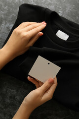 Female hands hold sweatshirt and blank tag on black table