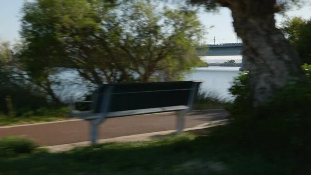 Approach major traffic bridge as you journey along tree lined bank of beautiful Canning River with walkers along foreground path.  Jetty visible