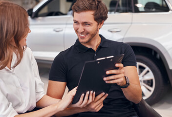 Fototapeta premium Happy couple reading contract in car dealership