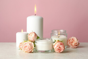 Scented candles and roses on white table against pink background