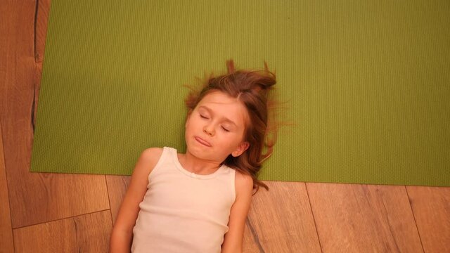 Cute little child girl lying on the floor and green yoga mat pretending to be asleep for fun