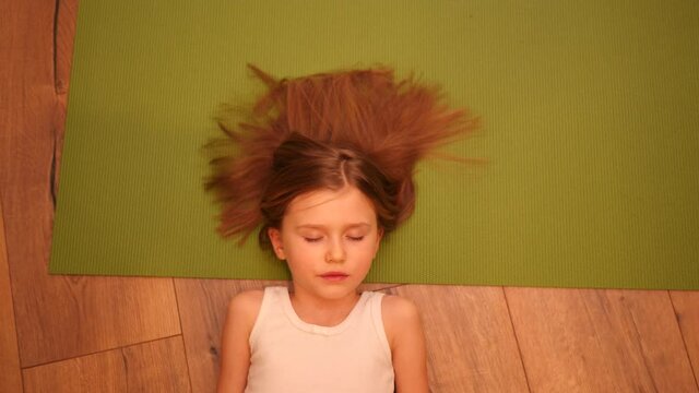 Cute little child girl lying on the floor and green yoga mat pretending to be asleep for fun