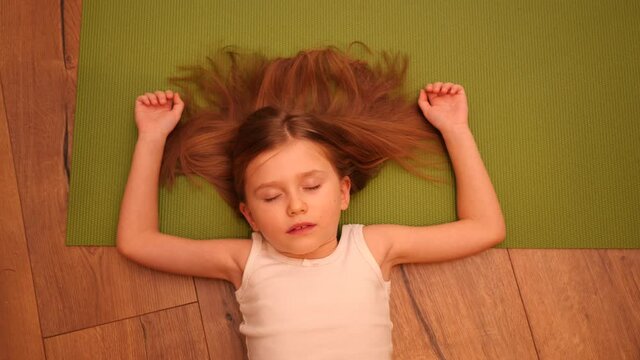 Cute little child girl lying on the floor and green yoga mat pretending to be asleep for fun