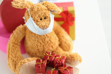 Soft toy in medical protective mask next to gifts