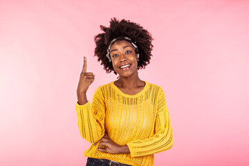Glad pleased African American woman keeps hands up and points fingers above. Happy dark skinned lady draws your attention to copy space, poses against pink background