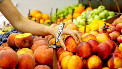 Young caucasian woman is choosing a ripe nectarines at supermarket. Close-up of female hands is taking peaches from shelf.