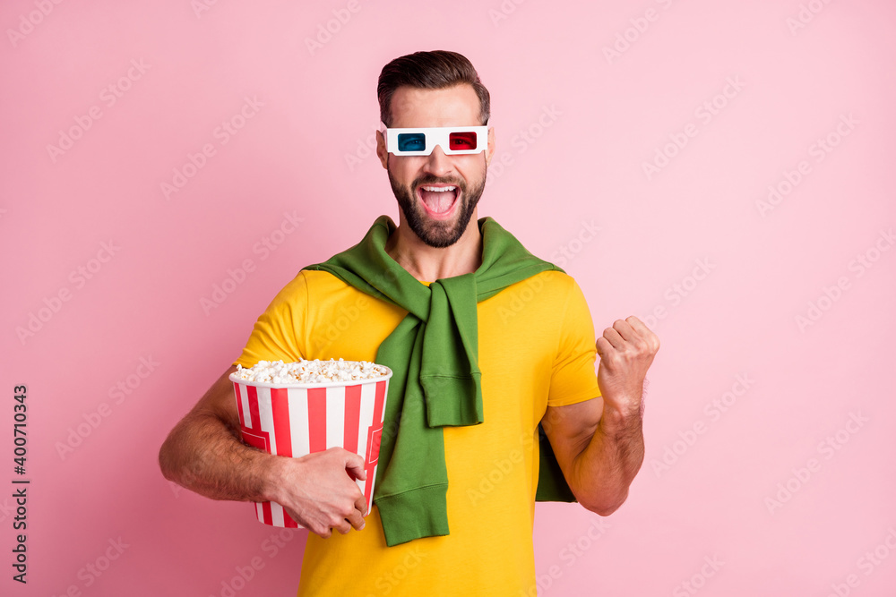 Sticker Photo of triumphant young handsome man raise fist hold pop corn watch tv isolated on pink color background