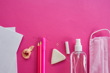 Flat lay schooling after the coronavirus pandemic, Back to school in a new reality, School supplies, protective mask and antiseptic on a pink background, space for text..