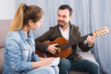 Positive young guitar tutor helping client to learn instrument