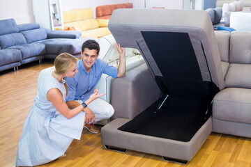 Obraz premium Family couple are choosing new sofa with a rising bottom in furniture store.