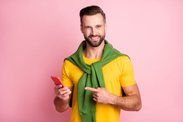 Photo of sweet cute young man dressed yellow t-shirt sweater shoulders pointing finger modern gadget isolated pink color background