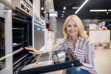 Fototapeta na wymiar Blonde customer choosing oven in a showroom and smiling
