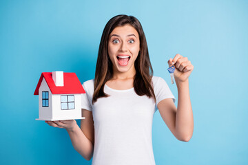 Photo of young shocked amazed smiling cheerful girl hold little house and keys isolated on blue...