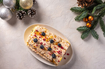 Homemade Meringue roll cake with cream, berries and almond on plate, selective focus, in the background Christmas tree branches with cones and toys, top view