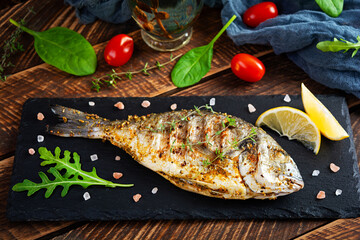 Grilled dorado fish on wooden background. Roasted seafish with spice and herbs