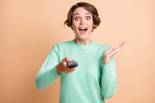 Photo of young attractive woman amazed excited shocked news watch tv hold remote control isolated over beige color background