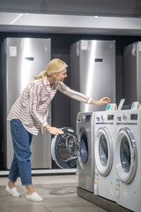 Woman in striped shirt choosing a washing machine in a showroom and looking interested