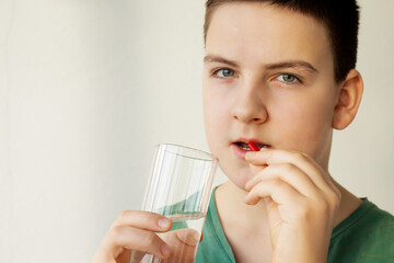 a boy (young man) holding a red capsule with medicine and a glass of water; health care concept, additives or vitamins, disease treatment