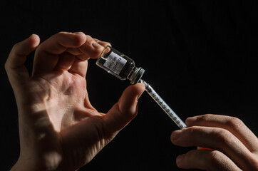 Ampoule with covid-19 vaccine and syringe for injection on black background