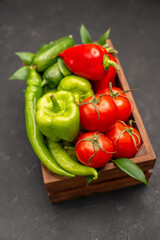 Vertical view of a vegetable basket with fresh tomatoes green and red peppers cucumber on dark background