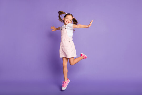 Full length of carefree happy small girl wear pink dress raise hands good mood isolated on violet color background