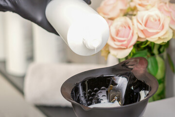 Hairdresser's hand mix hair dye in a black bowl in a beauty salon