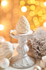 Dessert in the form of Christmas pine cone. Mini mousse pastry dessert covered with velour. Garland lamps bokeh on background. Modern european cake. French cuisine. Christmas theme. Copy space