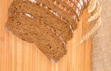 Sliced brown bread and wheat ears, fragment top view