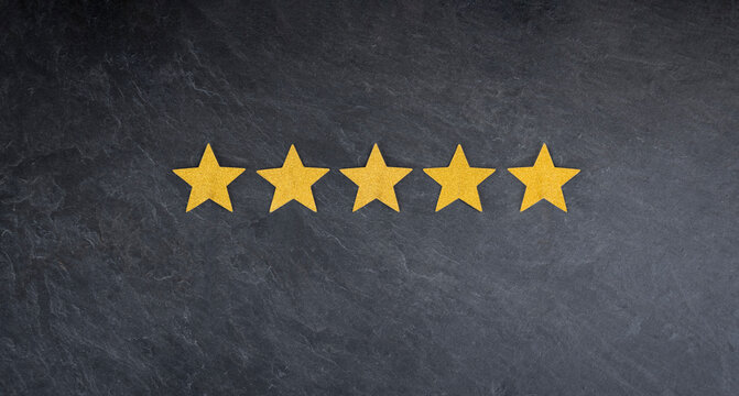 Five golden, glittering stars on a slate background as a symbol for a very good rating and high quality