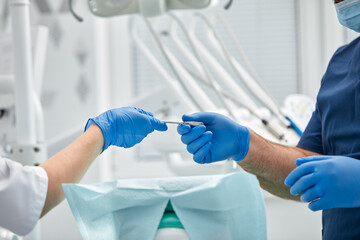 Close-up of the hands of a dentist and nurse surgeon over an operating room during a dental implant...