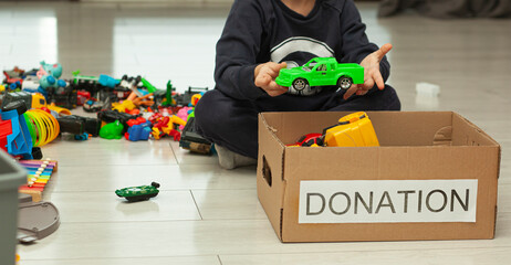 The boy is sorting his toys and puts toy car into the donation box