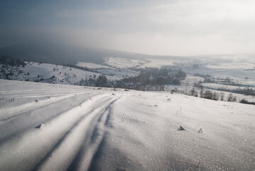 Car tracks on snow with a mountain village in a distanse. Somewhere in the Carpathians. 