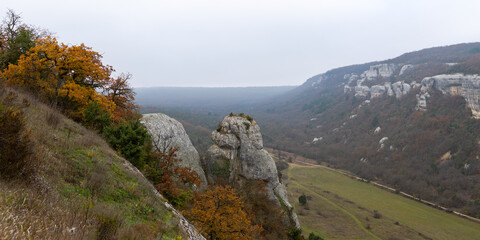 Mountains, autumn forest and fog. Beautiful morning in a mountain valley. Panoramic landscape of misty mountains with oak forest. The cave city of Eski-Kermen in the Bakhchisarai district of Crimea