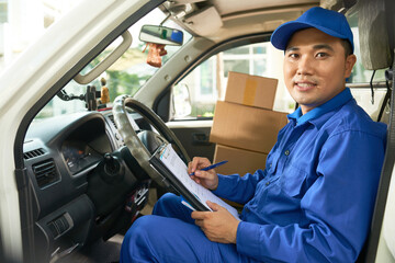 Portrait of Vietnamese develiry truck driver checking information in document before unloading...