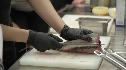 person in gloves cuts fish with a knife on the table