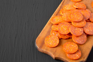 Italian Pepperoni Slices on a rustic wooden board on a black surface, side view. Copy space.