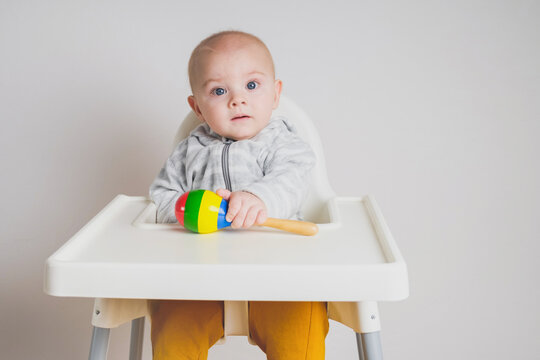 Cute Baby Boy Sitting In High Chair With Toy Against White Wall. Adorable Little Caucasian Infant Baby.