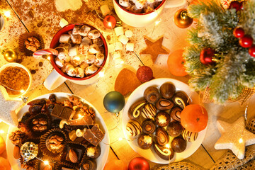 sweet food top view background for merry christmas or new year holiday decoration with night illumination - chocolate candies, tangerines, cookies, marshmallow and cocoa latte on white wood