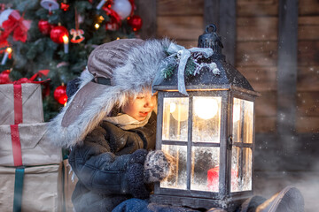 New Year's miracle. A little boy in winter clothes holds a Christmas lantern in his hands and looks at it. Outdoors, in winter.