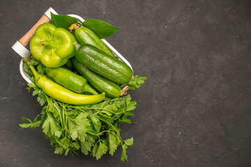 Close up view of a vegetable basket with a bunch of green and peppers cucumber on dark background