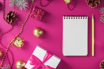 Notepad in holiday toys and decorations on pink christmas background.
