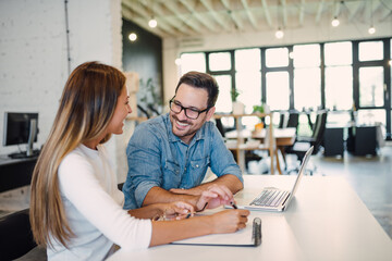 Two cheerful colleagues smiling while discussing something in modern office.