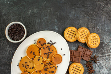 close up view of pancakes with a bowl of chocolate chips and cookies on grey ground