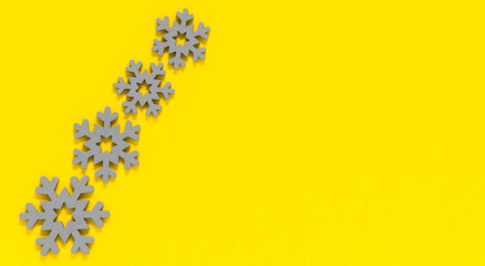 Grey wooden snowflakes on yellow background. Minimal winter backdrop in trendy colors of year 2021 illuminating yellow and ultimate gray. Copy space for text