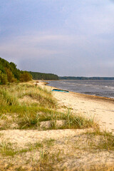 Coast of the Baltic Sea in Latvia, with pine trees on the sand dunes and an abandoned wooden boat.