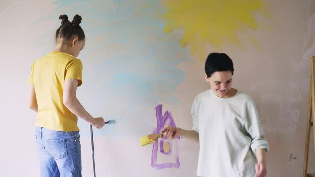 Family have fun while renovate room. Girl with mother paint face to each other against flat wall after relocation drawing images for kids birthday present during self isolation school holidays